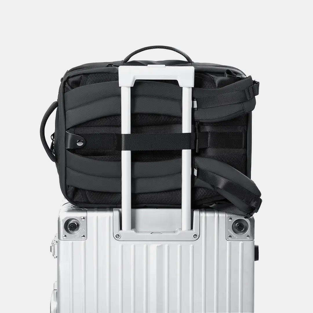 Close-up of the backpack's rear panel secured tightly to a rolling suitcase handle using the dedicated luggage pass-through strap.