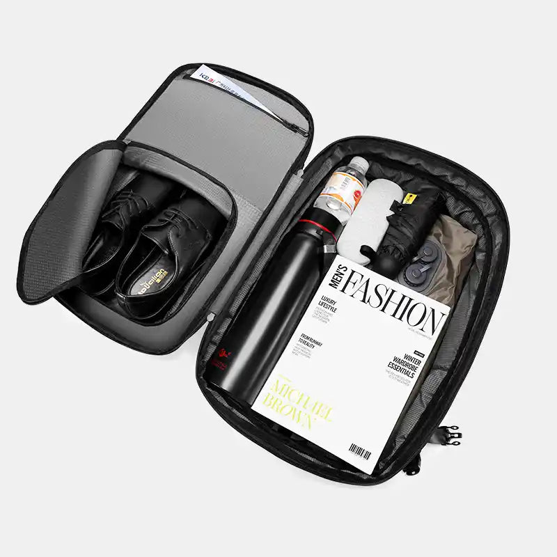 Open black travel bag with shoes, a bottle, and a magazine on a white background