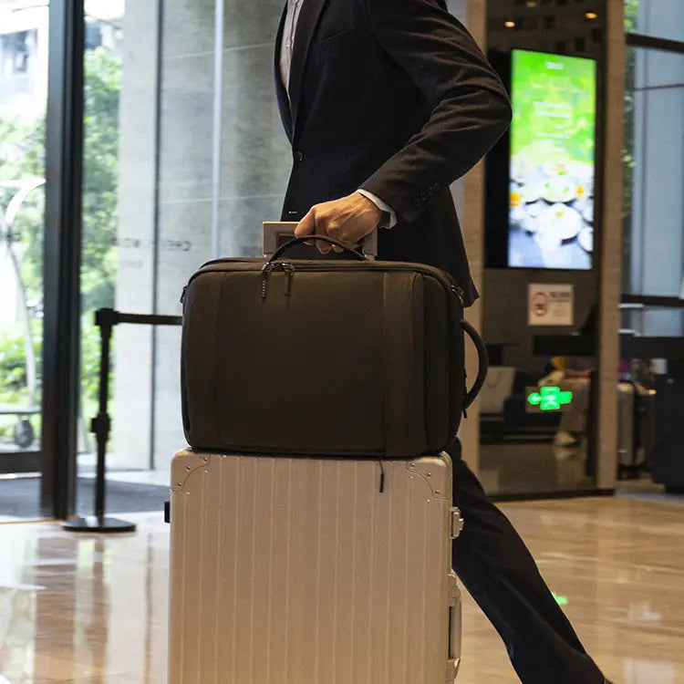 Business traveler carrying a black Cinomadist travel bag on a rolling suitcase