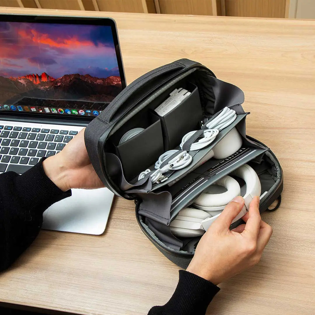Person organizing gadgets inside the Cinomadist tech pouch at a workspace, showing multi-layer compartments.
