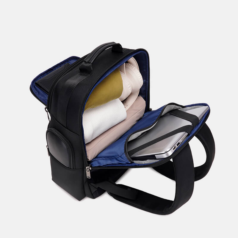 Black backpack with compartments containing a laptop, books, and clothing on a light gray background