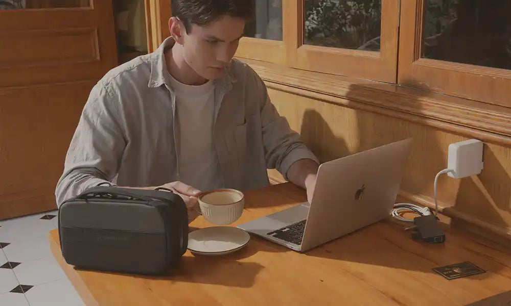 Person sitting at a desk with a laptop and backpack in a room with wooden cabinets.