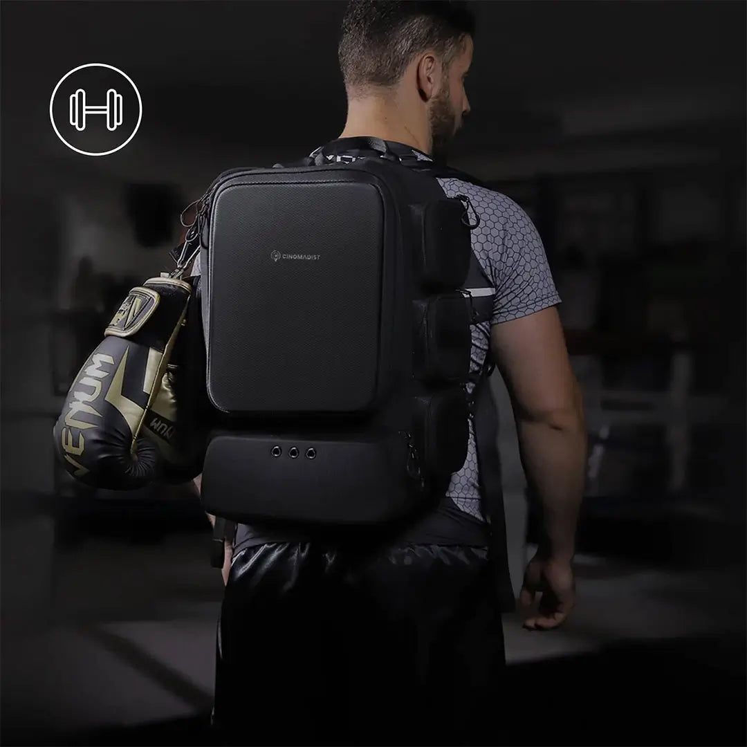 Man wearing a black backpack with boxing gloves on the ground, gym equipment in the background