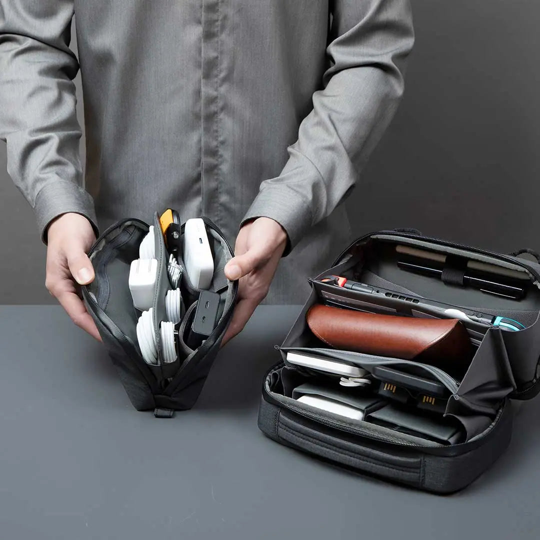 A person vertically organizing gadgets and cables inside a Cinomadist slim tech pouch with dual compartments.
