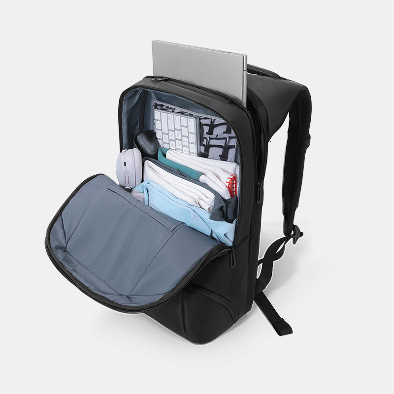 Black backpack with compartments containing a laptop, keyboard, and other items on a light gray background