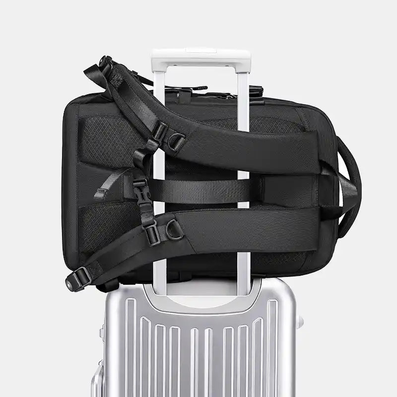 Black travel bag with straps on a silver suitcase against a white background