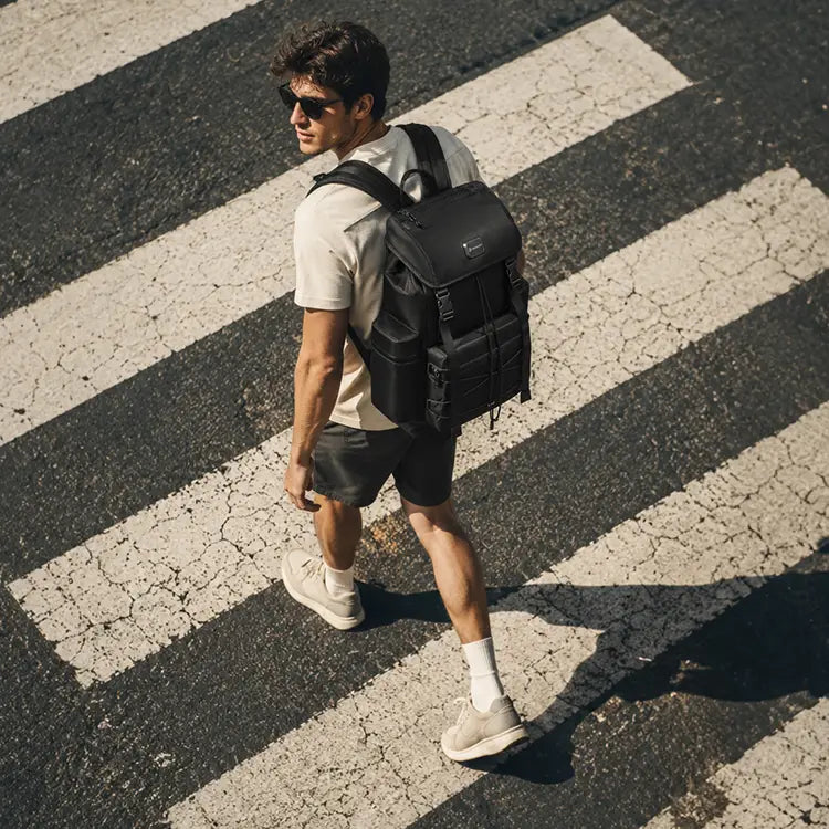 Man wearing a black Cinomadist travel backpack on a city crosswalk