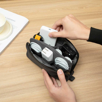 Hands placing charging accessories into a compact Cinomadist slim tech pouch on a wooden desk.