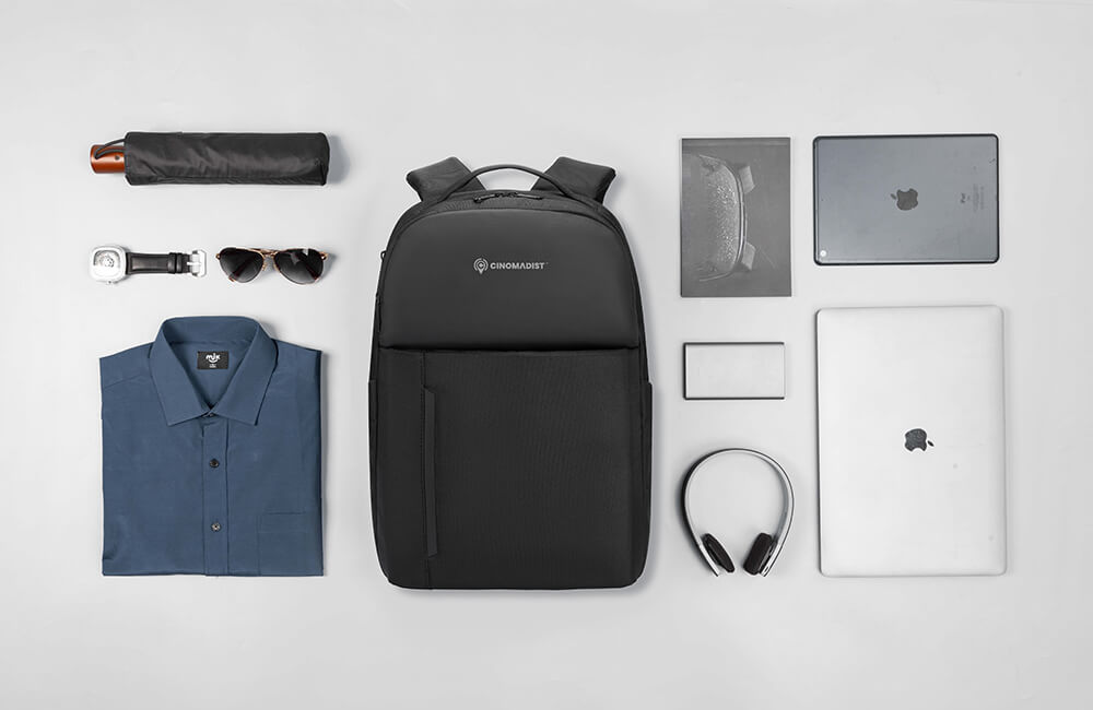 Black backpack with various items on a light gray background