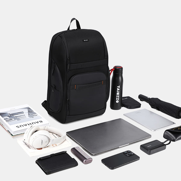 Black backpack with various items including a laptop, headphones, and a water bottle on a white background