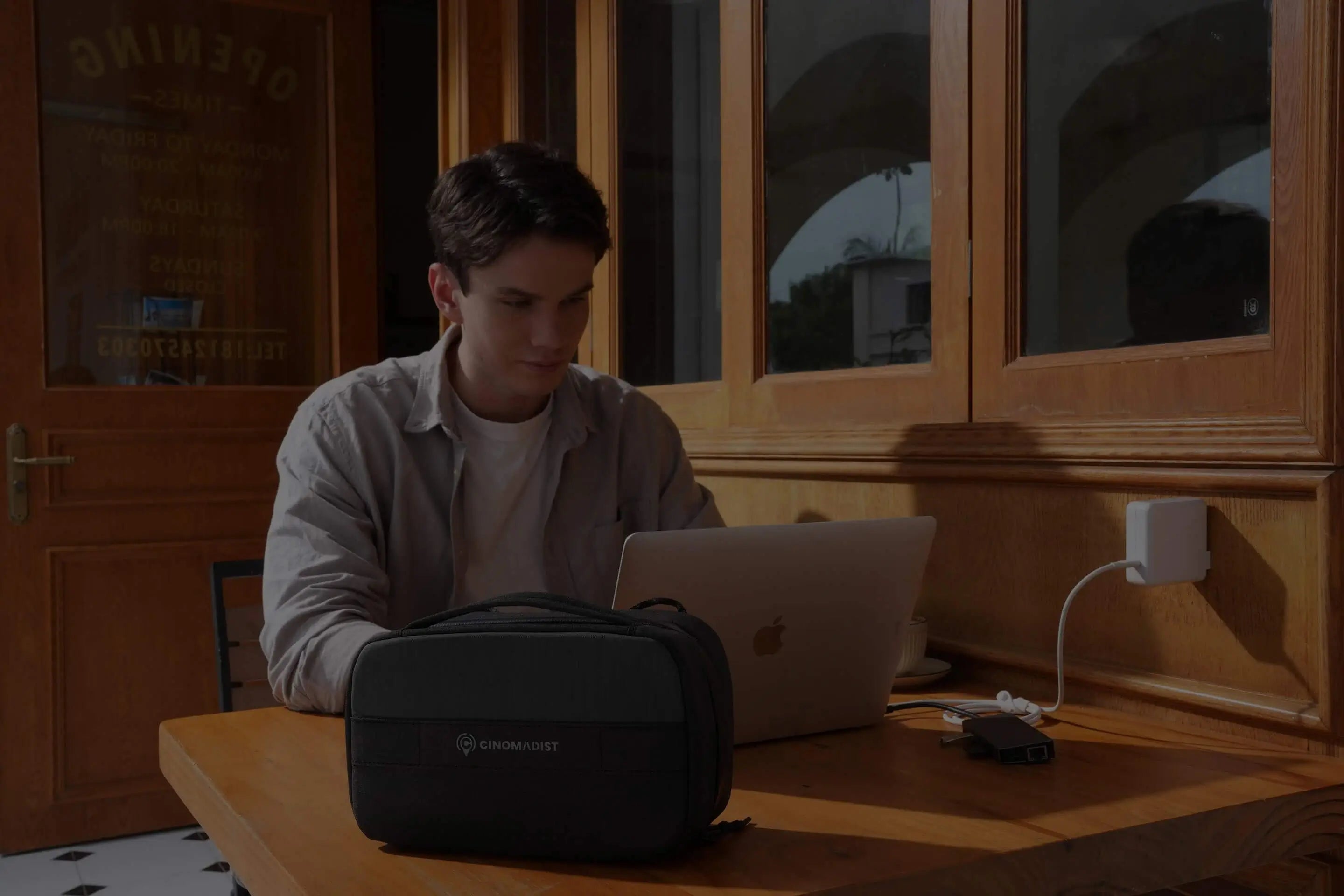 Person sitting at a desk with a laptop and backpack in a room with wooden cabinets.